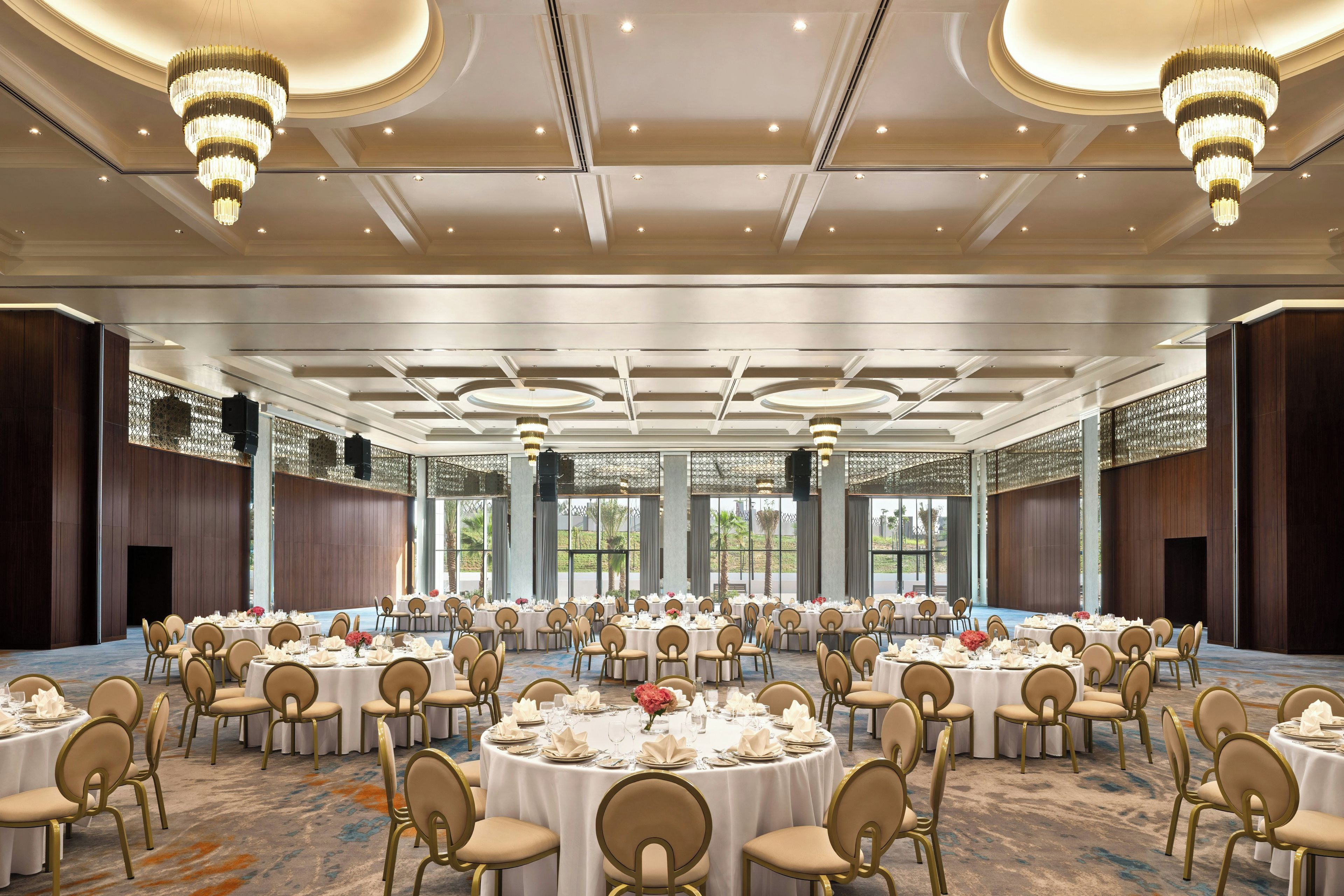 A large banquet hall with round tables, chairs, and chandeliers.