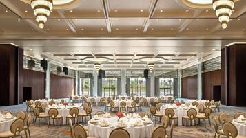 A large banquet hall with round tables, chairs, and chandeliers.