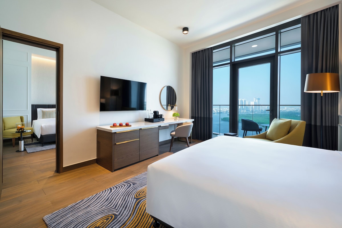A hotel room with a large bed, a desk, a TV, and a view of the city.