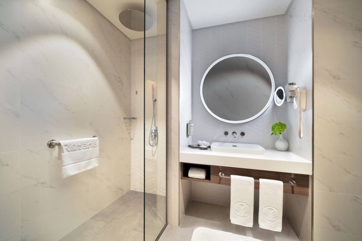 Un bagno moderno con box doccia in vetro, uno specchio rotondo, un lavandino bianco e una piccola pianta.