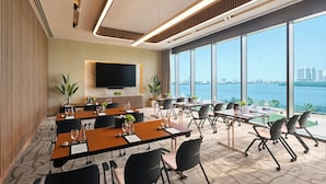 A modern conference room with large windows, a flat-screen TV, and a view of the city and water. - Rotana Ras Al Khaimah - The Mangroves (Ras Al Khaimah)