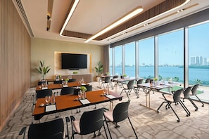 A modern conference room with large windows, a flat-screen TV, and a view of the city and water. - Rotana Ras Al Khaimah - The Mangroves (Ras Al Khaimah)