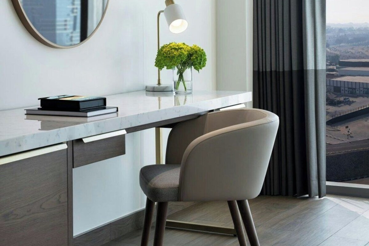 A modern office space with a desk, chair, lamp, and a view through large windows.