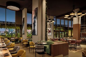 A modern restaurant interior with high ceilings, large windows, and a variety of seating arrangements including tables and booths. - Rotana Ras Al Khaimah - The Mangroves (Ras Al Khaimah)