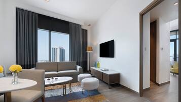 Una habitación de hotel moderna con sofá, una mesa de comedor, televisor montado en la pared y vistas a la ciudad.