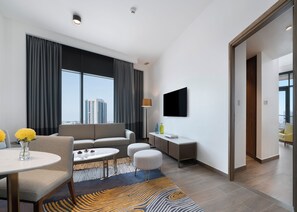 Una camera d'hotel moderna con divano, tavolo da pranzo, TV a parete e vista sulla città.