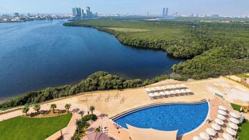 A resort with a swimming pool, beach area, and views of a river and city skyline.
