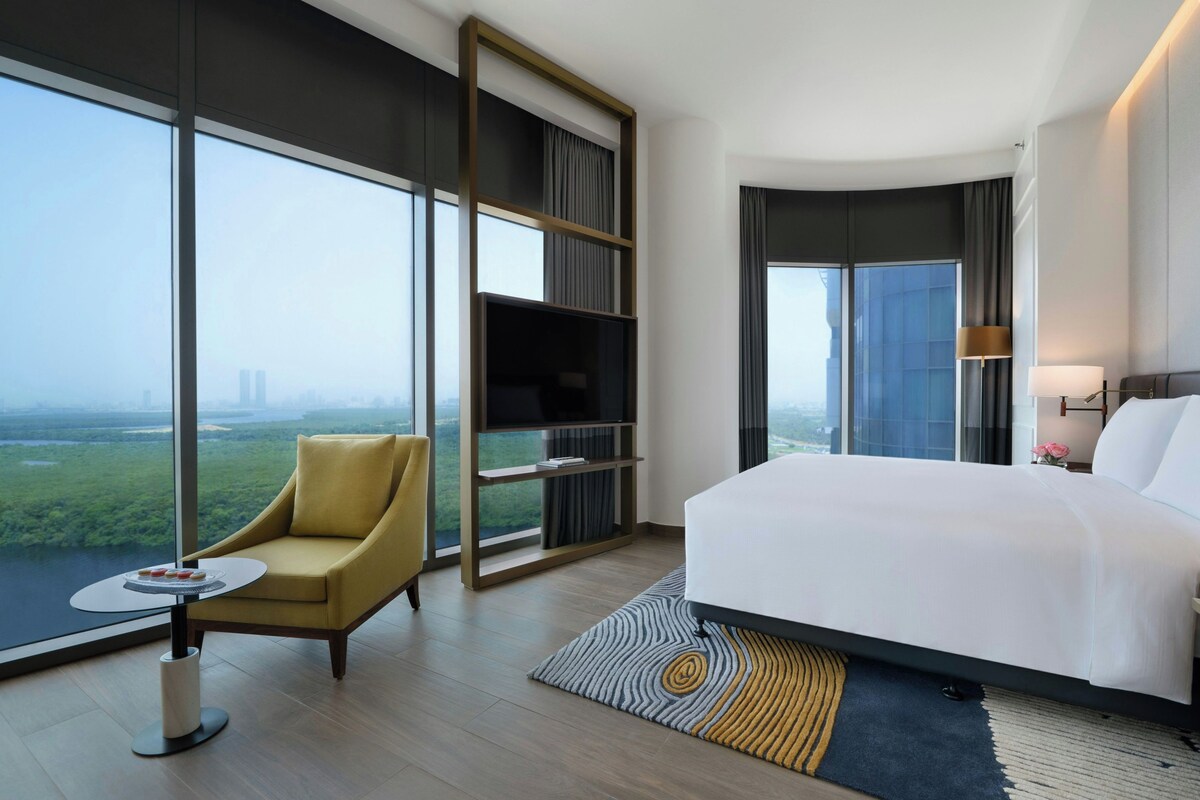 A hotel room with a large bed, a seating area with a chair, a small table, and a TV.