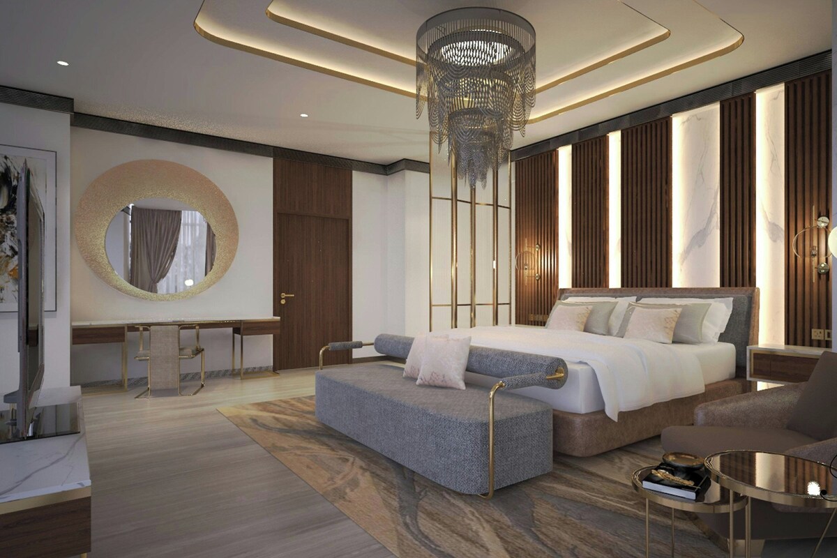 A modern bedroom with a large bed, a sitting area, a round mirror, and a decorative chandelier.