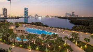 A resort with a swimming pool, palm trees, and a city skyline in the background.