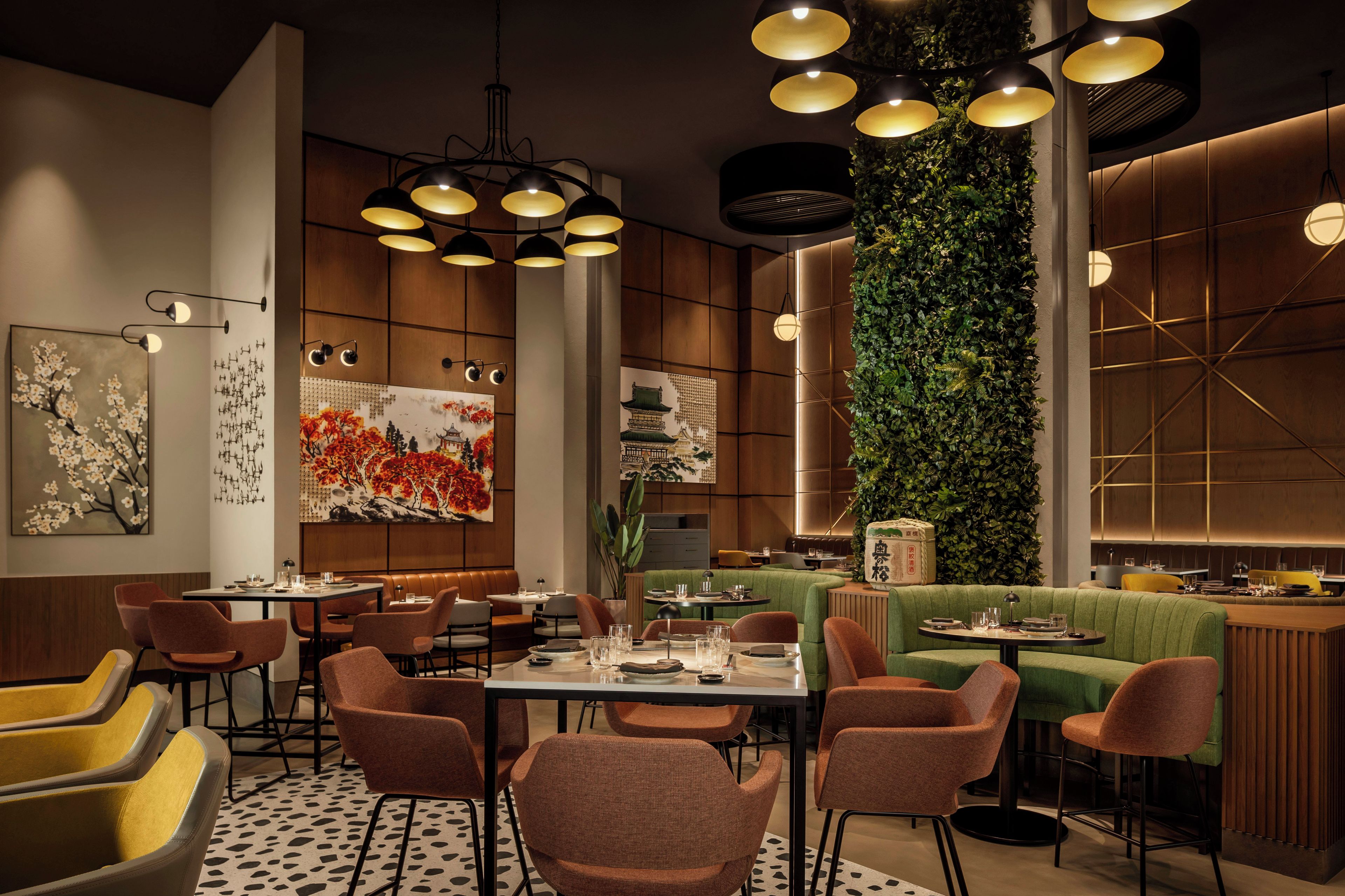 A modern restaurant interior with high ceilings, pendant lighting, and a green vertical garden wall.