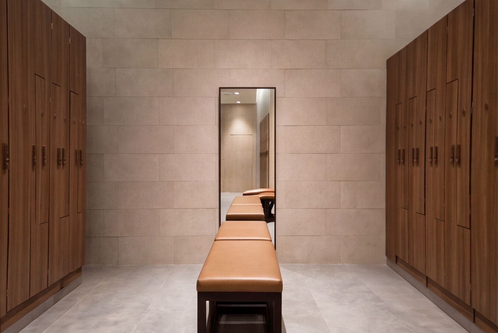 Un pasillo con taquillas de madera, un banco y un espejo que refleja una habitación.