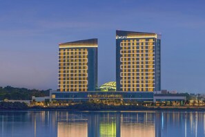 Egy modern hotel két feltűnő toronnyal, előtte egy tükröződő vízfelülettel, és a bal torony tetején egy jellegzetes, zöld színű építmény található.