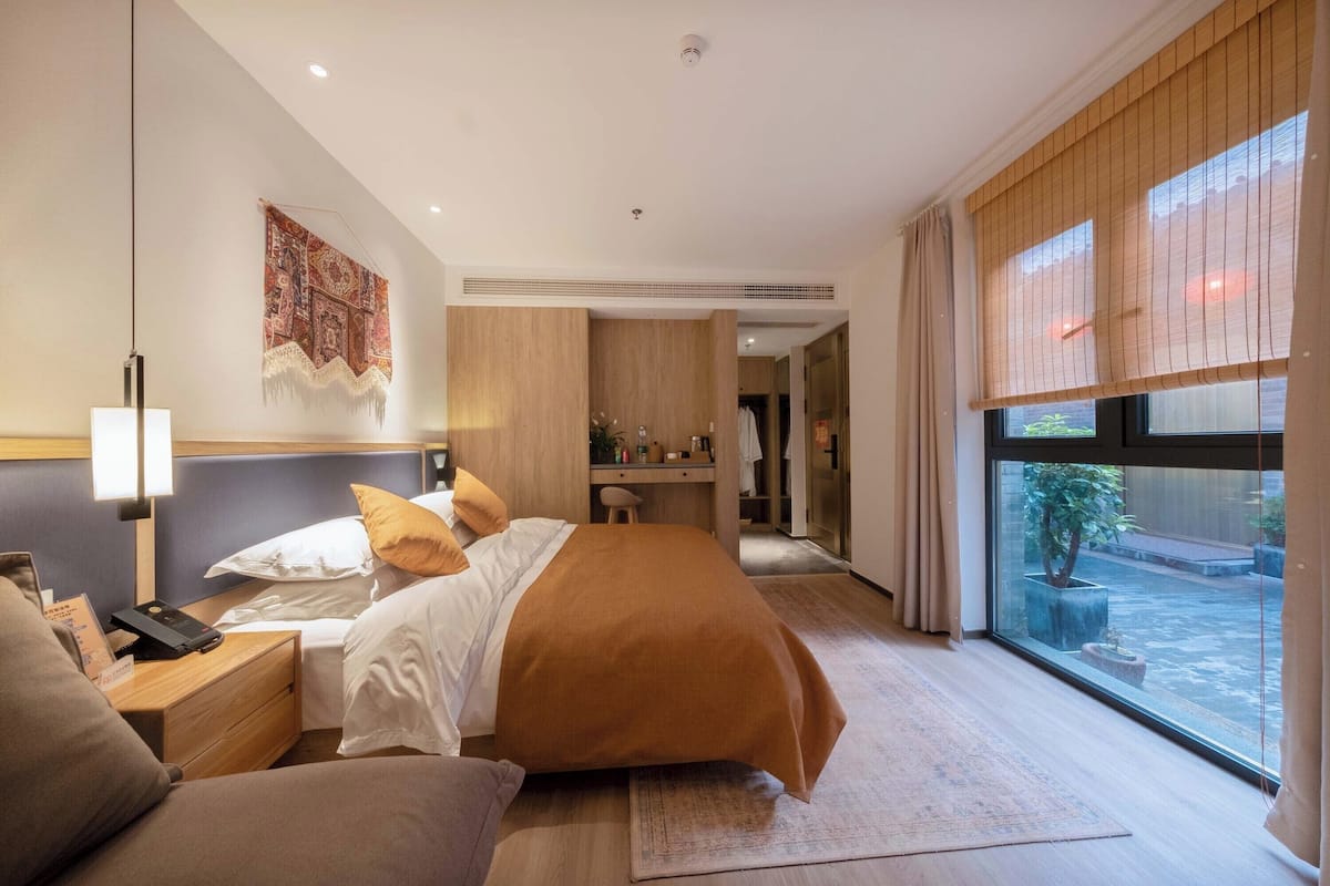 Habitación de hotel moderna con una cama grande, mesitas de noche, un escritorio y vistas al exterior.