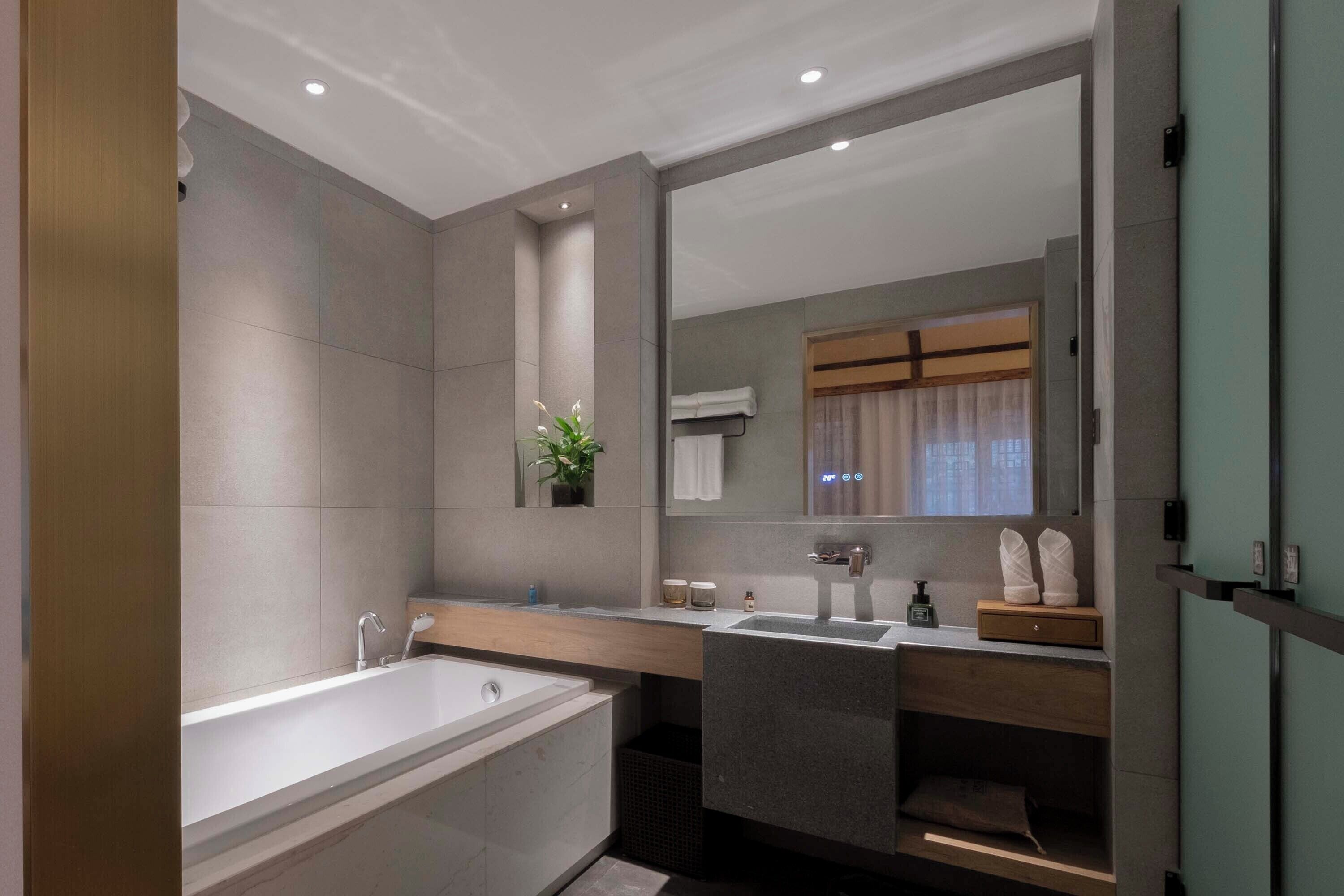 Un baño moderno con bañera, lavamanos y un espejo grande.