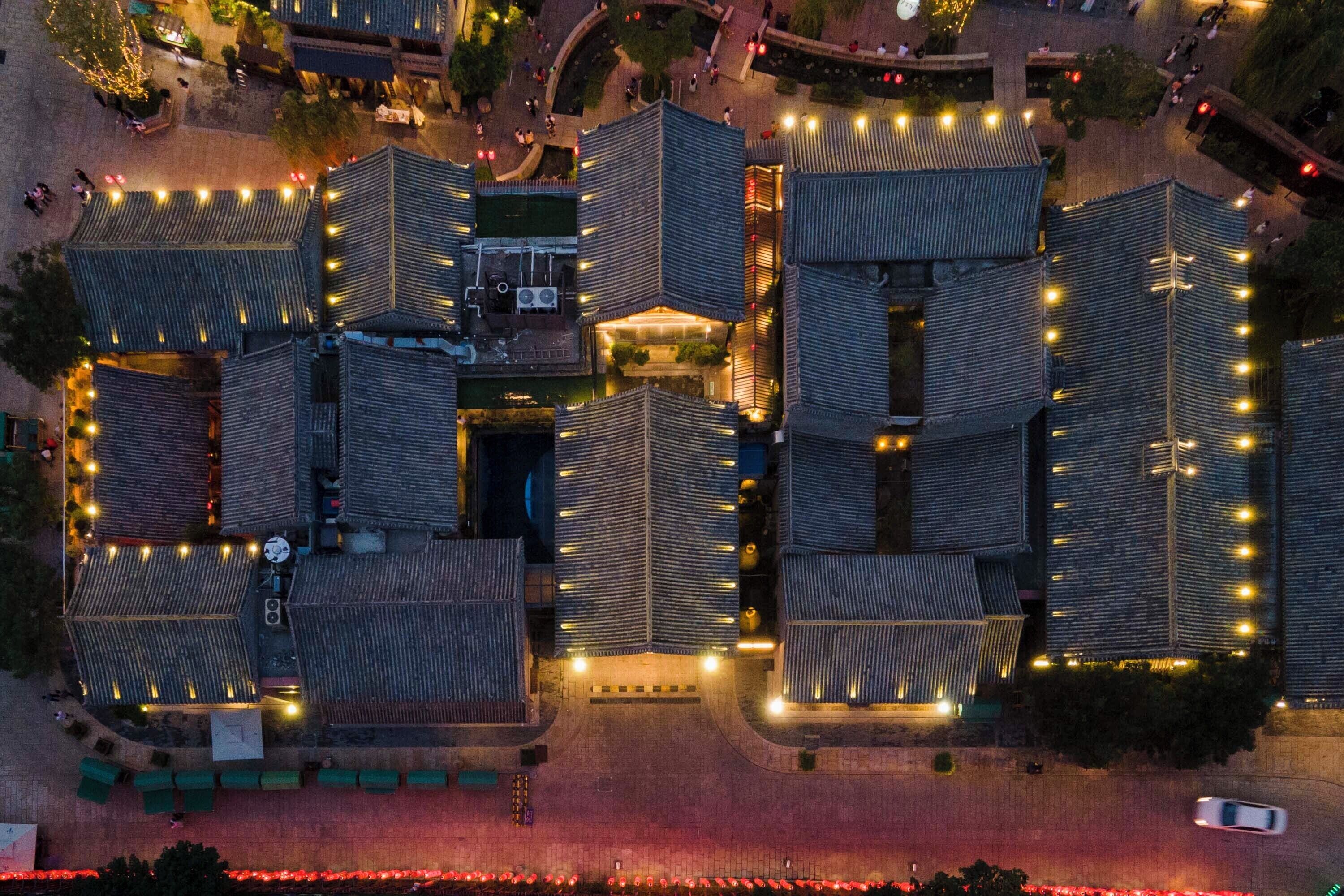 Vista aérea de un hotel con varias edificaciones, cada una con un perfil de techo diferente y rodeado de un perímetro bien iluminado.