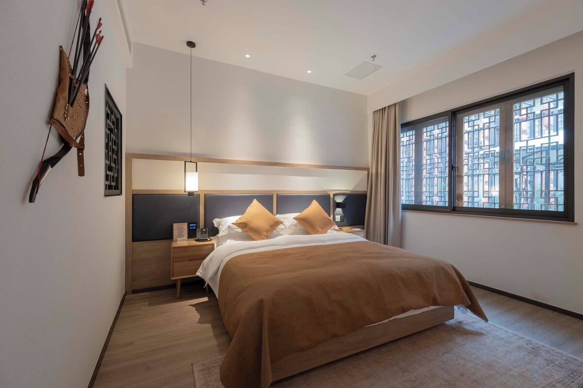 Un dormitorio moderno con una cama grande, cabecero de madera, mesitas de noche y una ventana con vistas a edificios.