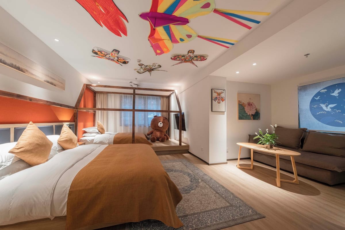 Una habitación de hotel moderna con una cama grande, un sofá, una mesita pequeña y un techo con decoraciones coloridas.