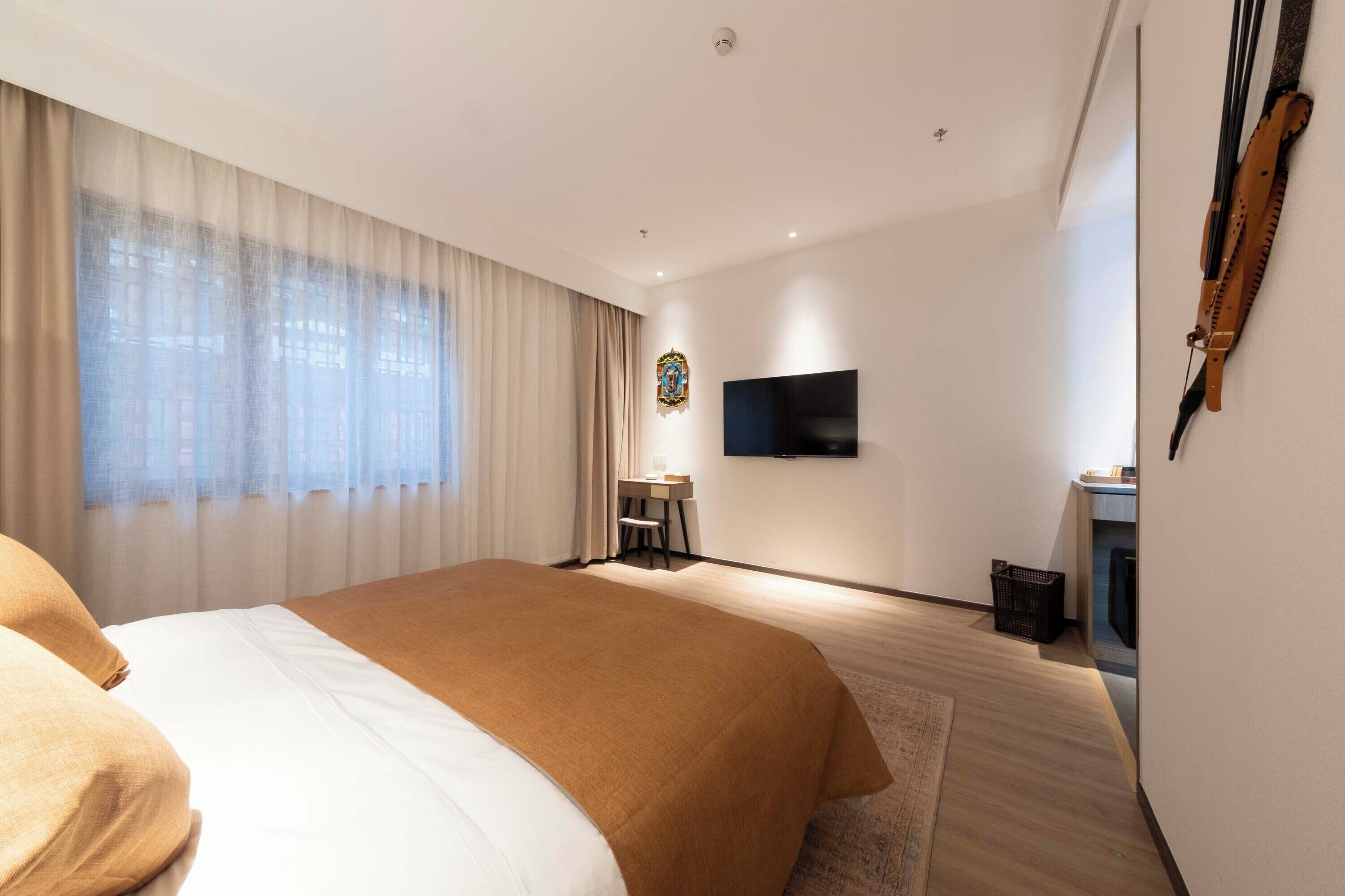 Habitación de hotel con una cama grande, un escritorio, un televisor montado en la pared y una ventana con cortinas.