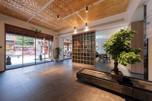 Una hall moderna con soffitto in legno, una reception, un'ampia pianta in vaso e una libreria.