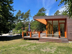 A modern wooden cabin with a deck, surrounded by trees and a clear sky. - 5 Star Holiday Home in Gotlands Tofta (Gotlands Tofta)