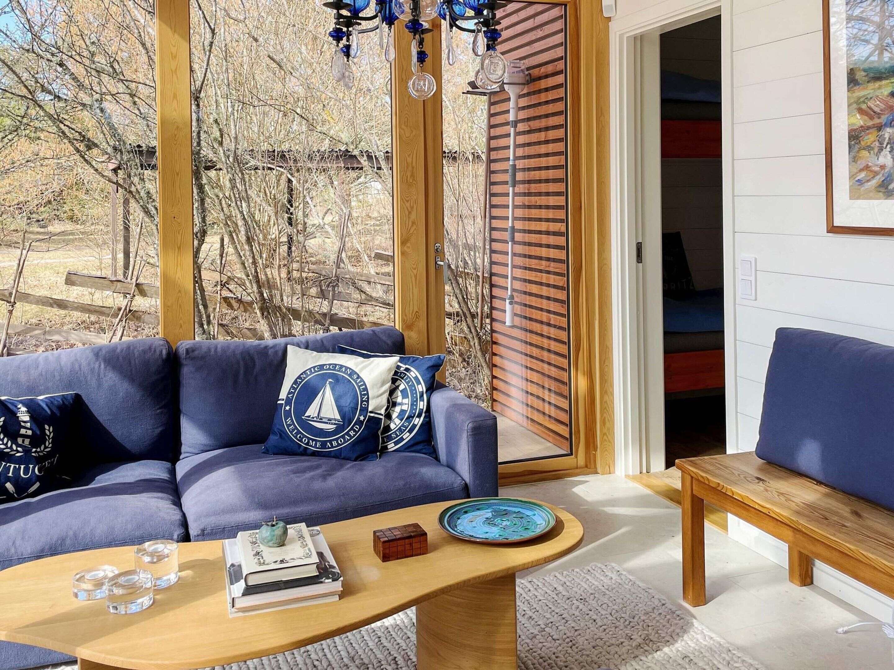 A modern living room with a blue sofa, wooden coffee table, and a view of a wooden deck and trees.
