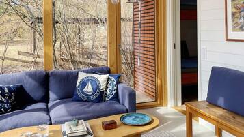 A modern living room with a blue sofa, wooden coffee table, and a view of a wooden deck and trees.