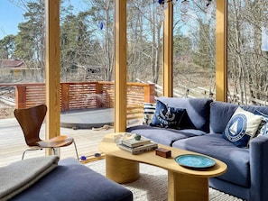 A modern living room with a blue sofa, wooden coffee table, and a view of a deck and trees. - 5 Star Holiday Home in Gotlands Tofta (Gotlands Tofta)