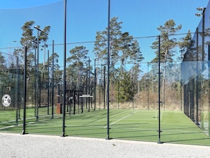 An outdoor tennis court with a net, surrounded by a fence, and trees in the background.