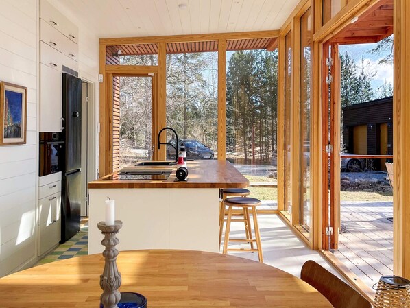 Una cocina moderna con una isla de madera, un área de comedor con una mesa y taburetes, y ventanas amplias que ofrecen vistas al exterior.