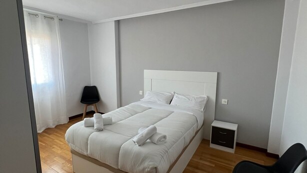 Un dormitorio moderno con una cama grande, una mesita de noche, una silla y un pequeño aparador.