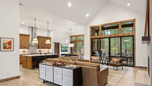 A spacious living area with a large sofa, a dining table, and a kitchen in the background. - Luxe Caldera Escape w/ Forest Views, Private Hot Tub, Sauna, Game Room, Seasonal Pool, Bikes & More! (Bend)