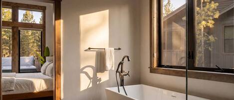 A modern bathroom with a freestanding bathtub, a towel rack, and a window with a view of trees.
