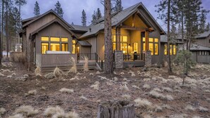 A modern log cabin with large windows and a stone foundation, surrounded by a forested area. - Luxe Caldera Escape w/ Forest Views, Private Hot Tub, Sauna, Game Room, Seasonal Pool, Bikes & More! (Bend)