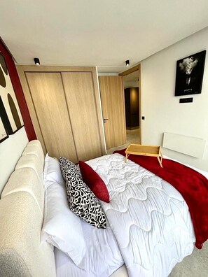 A bedroom with a bed, a wooden wardrobe, a bedside table, and a wall-mounted artwork. - À 2 Pas Du Tram | Studio Central • Parking - Free transfer - WiFi (Casablanca)