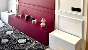 Un salon moderne avec un mur d’accent rouge, un téléviseur fixé au mur et une console blanche agrémentée d’objets décoratifs.