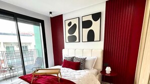 Une chambre moderne avec un grand lit, une petite table de chevet et une vue sur le balcon extérieur.