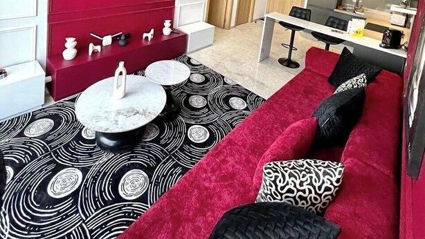 Un salon moderne avec un canapé rouge, un tapis à motifs noir et blanc, une table basse et un panneau Netflix fixé au mur.
