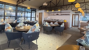 A spacious dining area with high ceilings and exposed beams, featuring round tables with blue upholstered chairs and patterned cushions. - Divine OAK Stay  (Pildi)