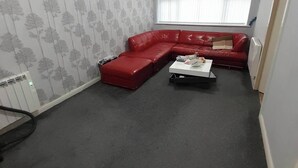 A living room with a red sectional sofa, a small white coffee table, and a radiator. - Room-eco-cottage Manchester (Manchester)