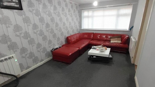 A living room with a red sectional sofa, a small white table, and a radiator. - Room-eco-cottage Manchester (Manchester)