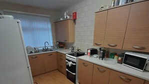 A compact kitchen with wooden cabinets, a stove, a microwave, and a refrigerator. - Room-eco-cottage Manchester (Manchester)