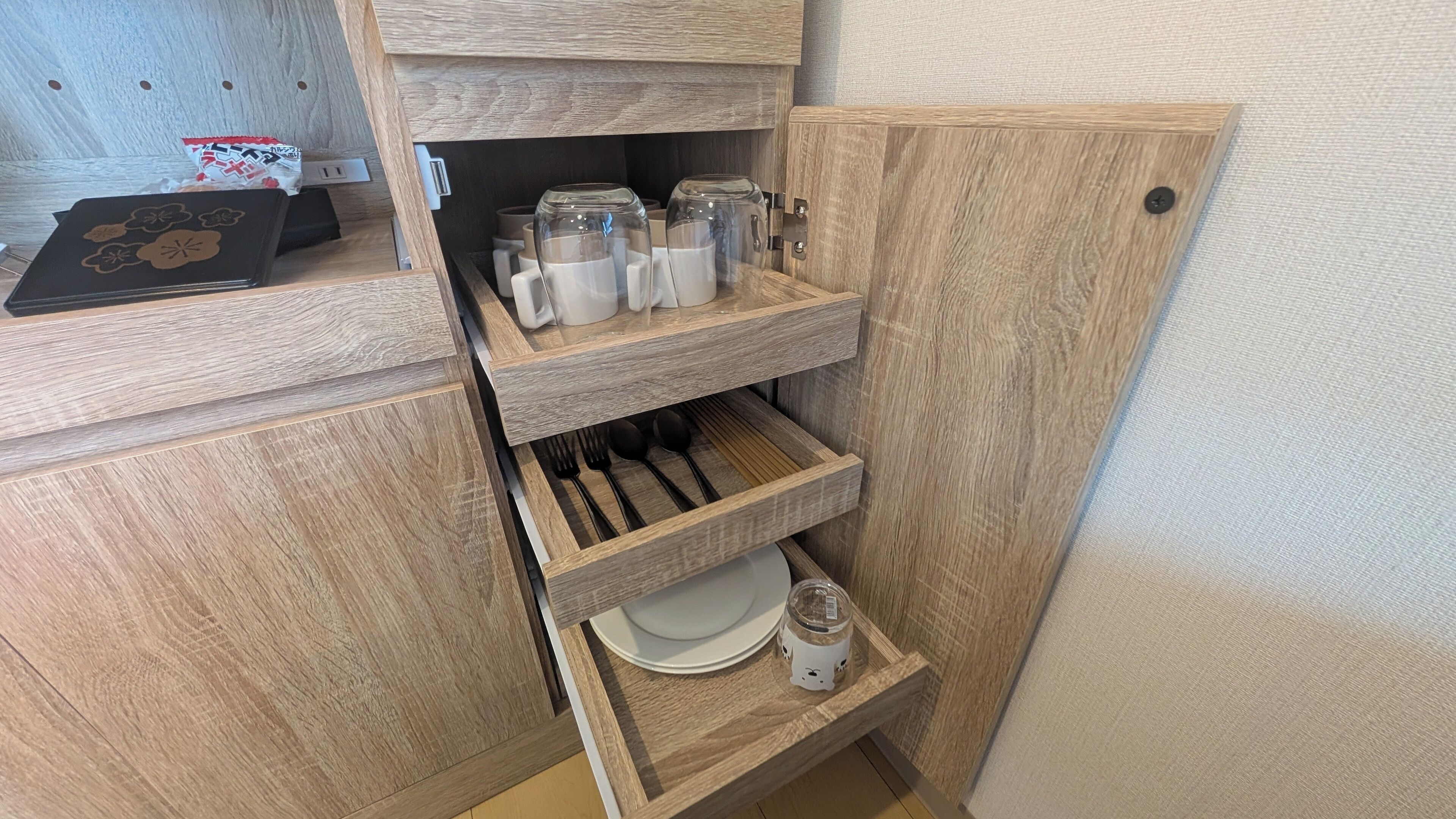 Una cocina compacta con armarios de madera, una cafetera integrada y una pequeña estantería con un plato y un frasco.