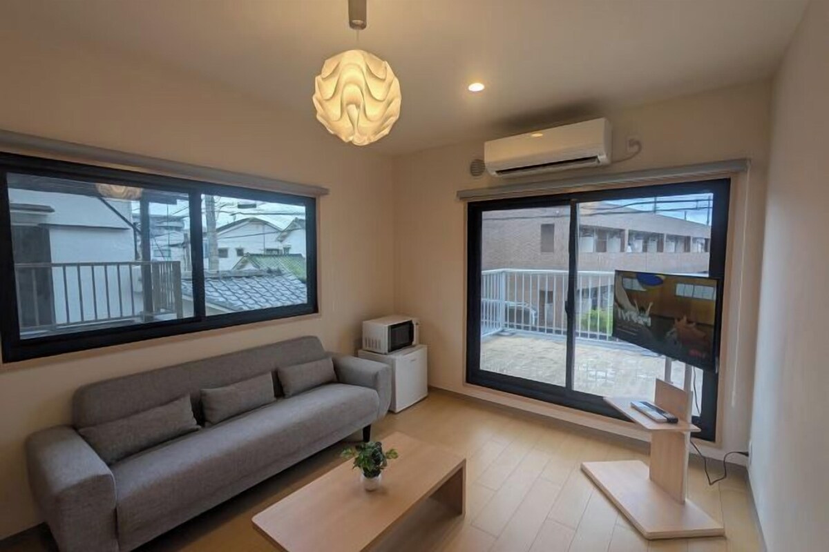 A modern living room with a sofa, a coffee table, and a TV. There is a large window and an air conditioning unit.
