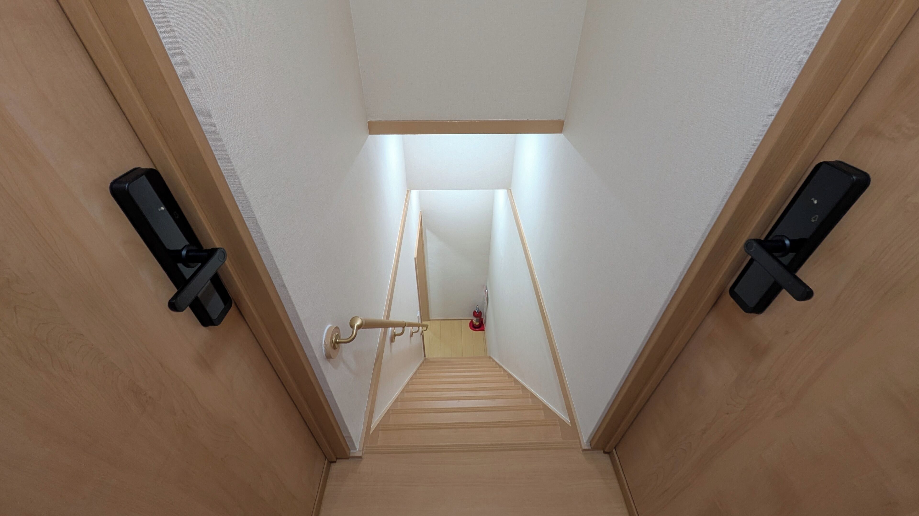 Un escalier étroit aux murs en bois et au plafond blanc, menant à une pièce dont la porte se trouve en haut.