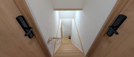 Un escalier étroit aux murs en bois et au plafond blanc, menant à une pièce dont la porte se trouve en haut.