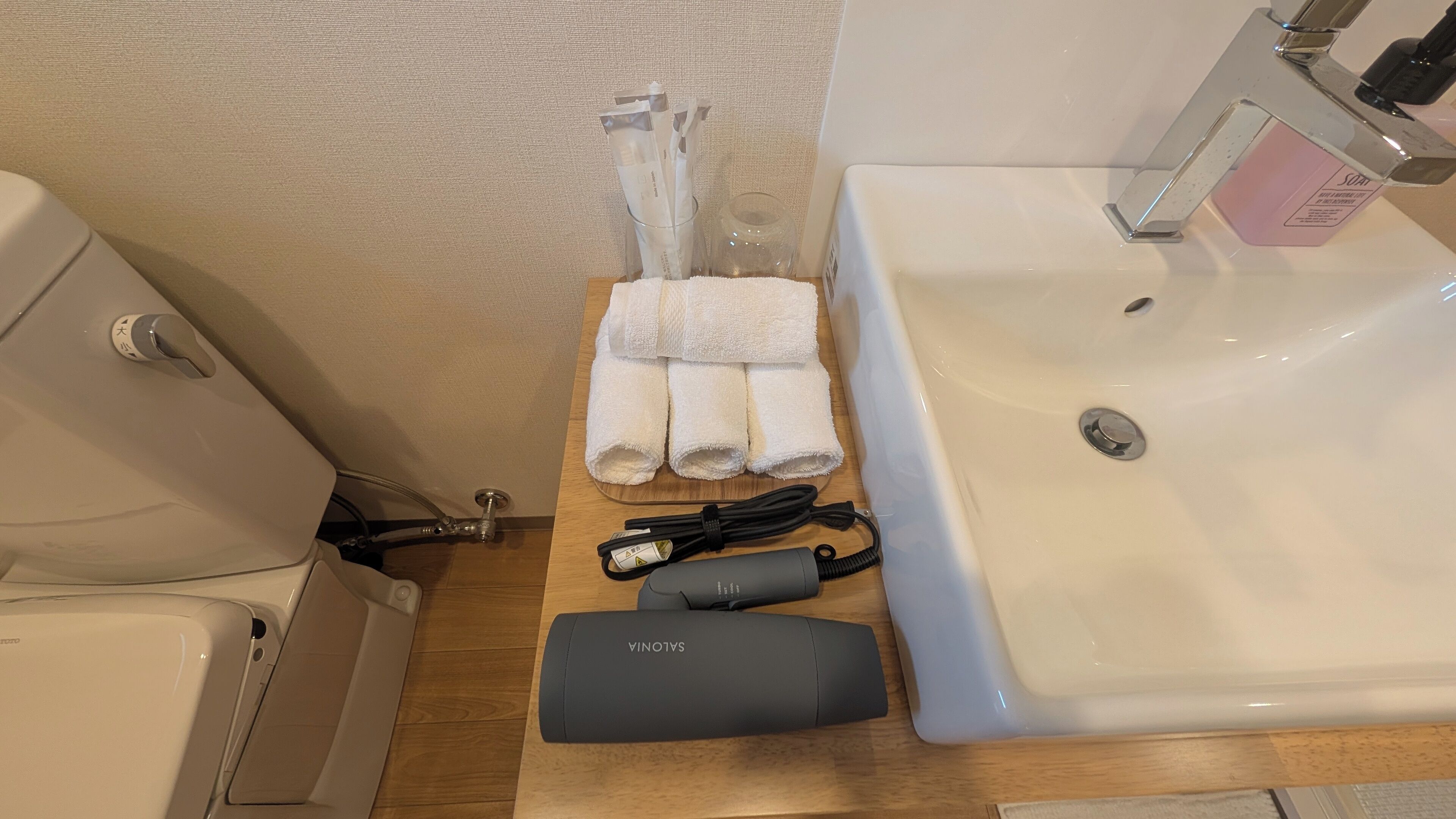 Un bagno con lavandino, porta asciugamani, un contenitore di vetro e asciugacapelli sul ripiano.