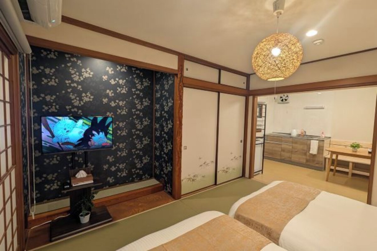 A traditional Japanese-style room with tatami flooring, a television, a dining area, and sliding doors.