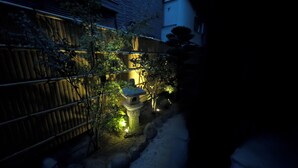 A dimly lit garden area with a stone lantern and bamboo fence. - Dream Stays SORA (Izumisano)