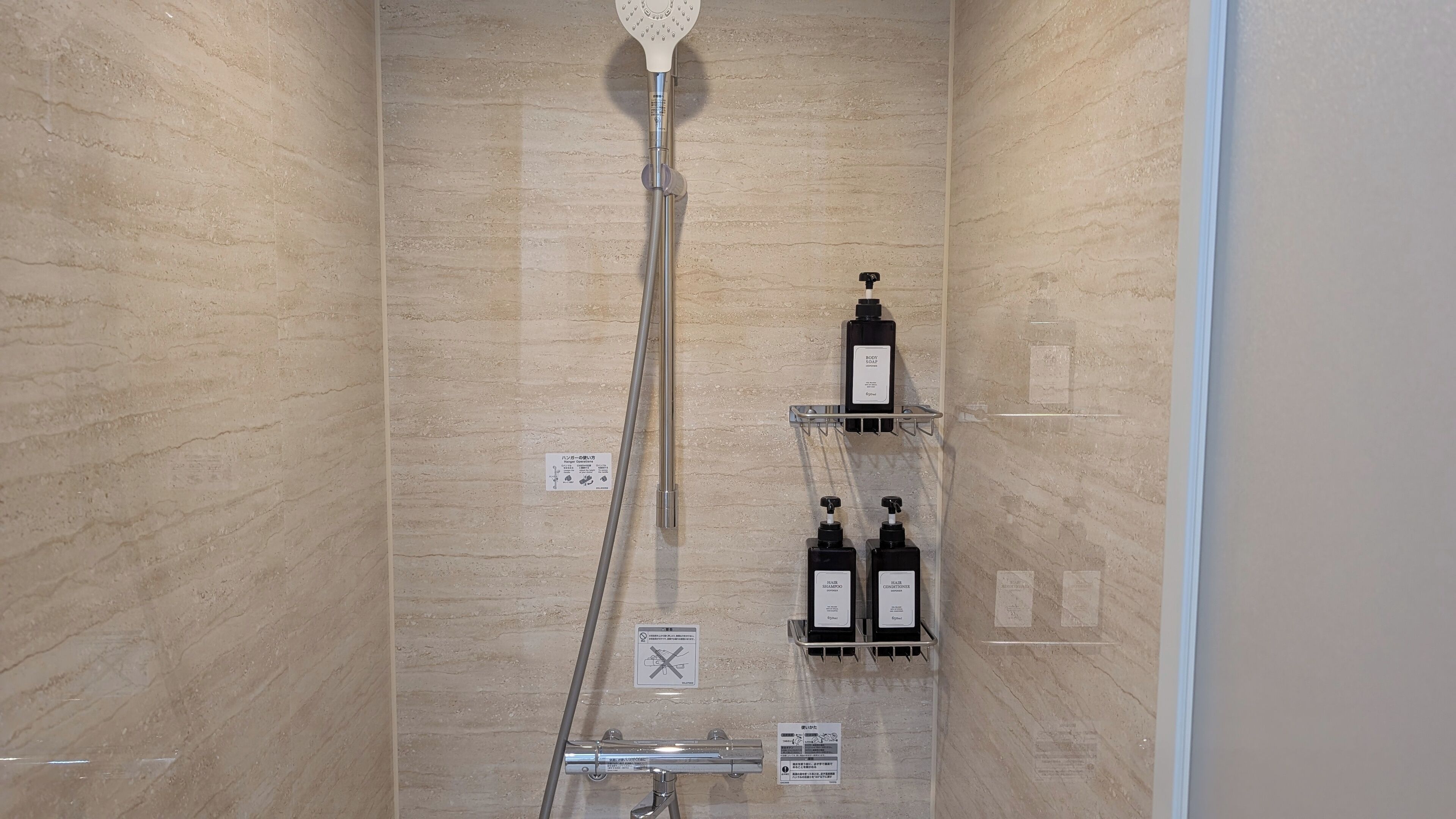 Un baño con ducha, dos repisas con artículos de aseo y un revestimiento de azulejos.